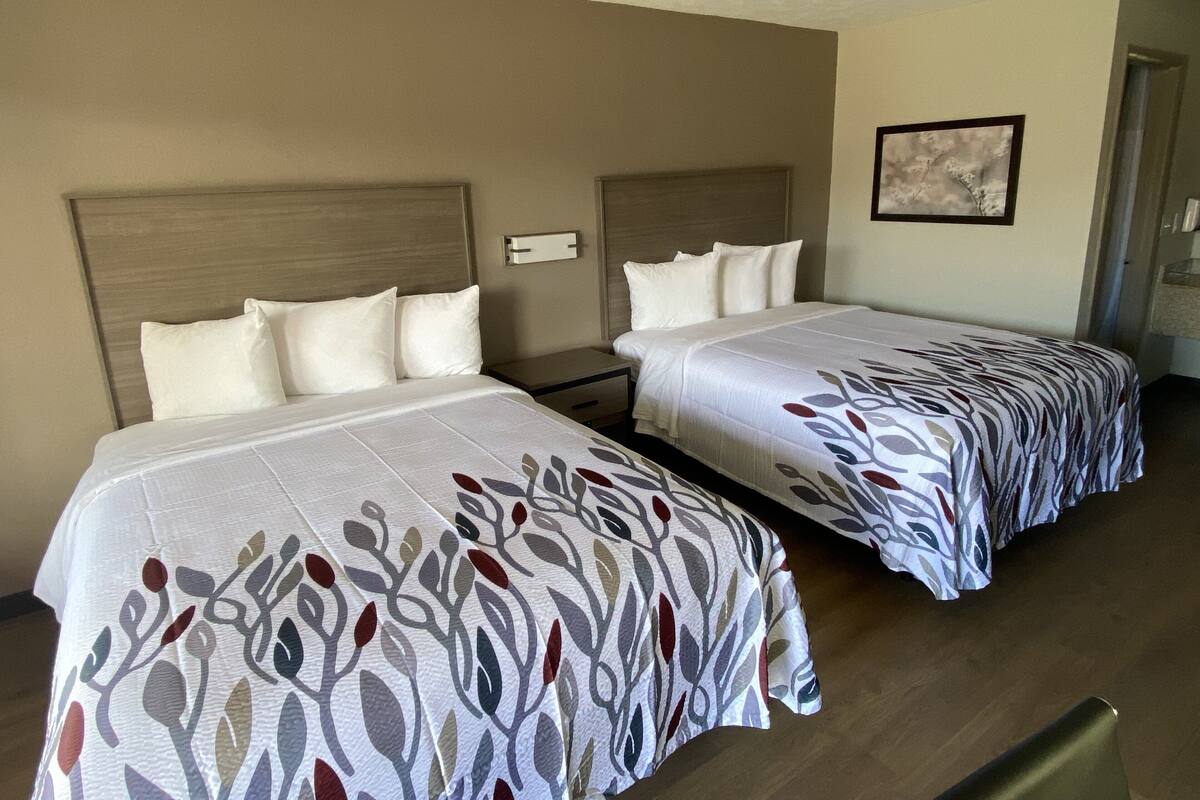 A hotel room with two beds, each with a headboard and pillows.