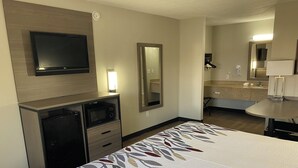 A hotel room with a bed, a TV mounted on the wall, a desk with a microwave, and a bathroom visible through an open door. - Red Roof Inn Jacksonville, AL  (Jacksonville)