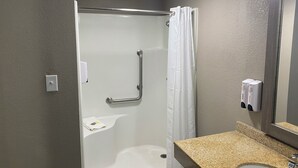 A bathroom with a shower, grab bar, towel rack, and a sink with a mirror. - Red Roof Inn Jacksonville, AL  (Jacksonville)