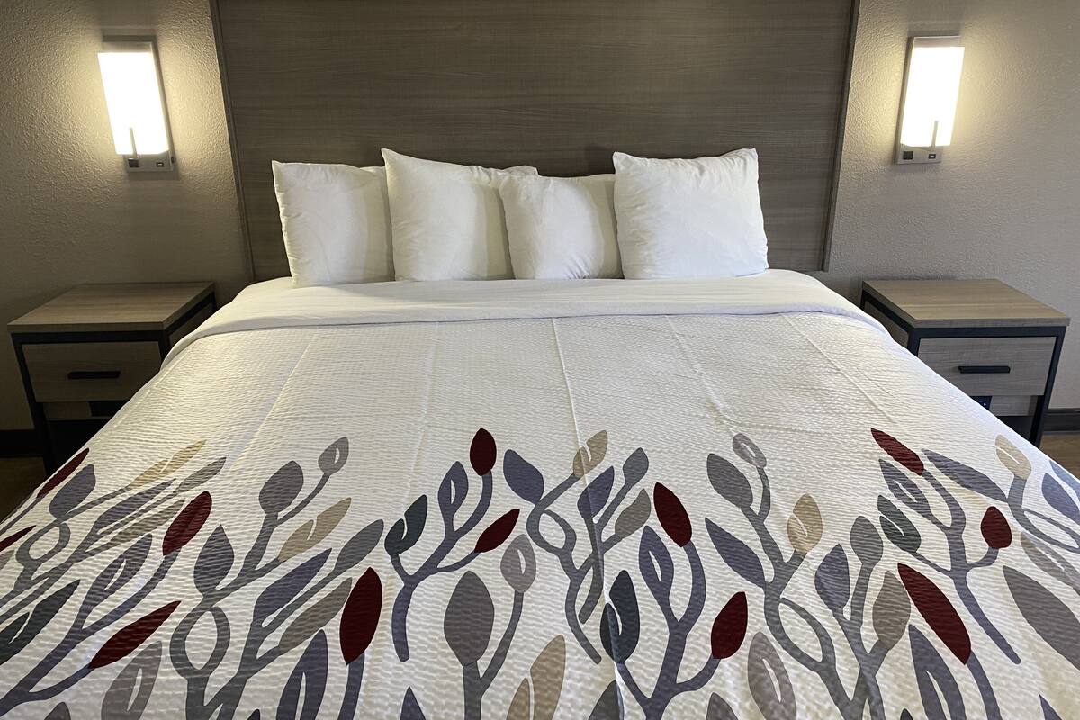 A neatly made bed with a patterned bedspread, two bedside tables, and wall-mounted lights.