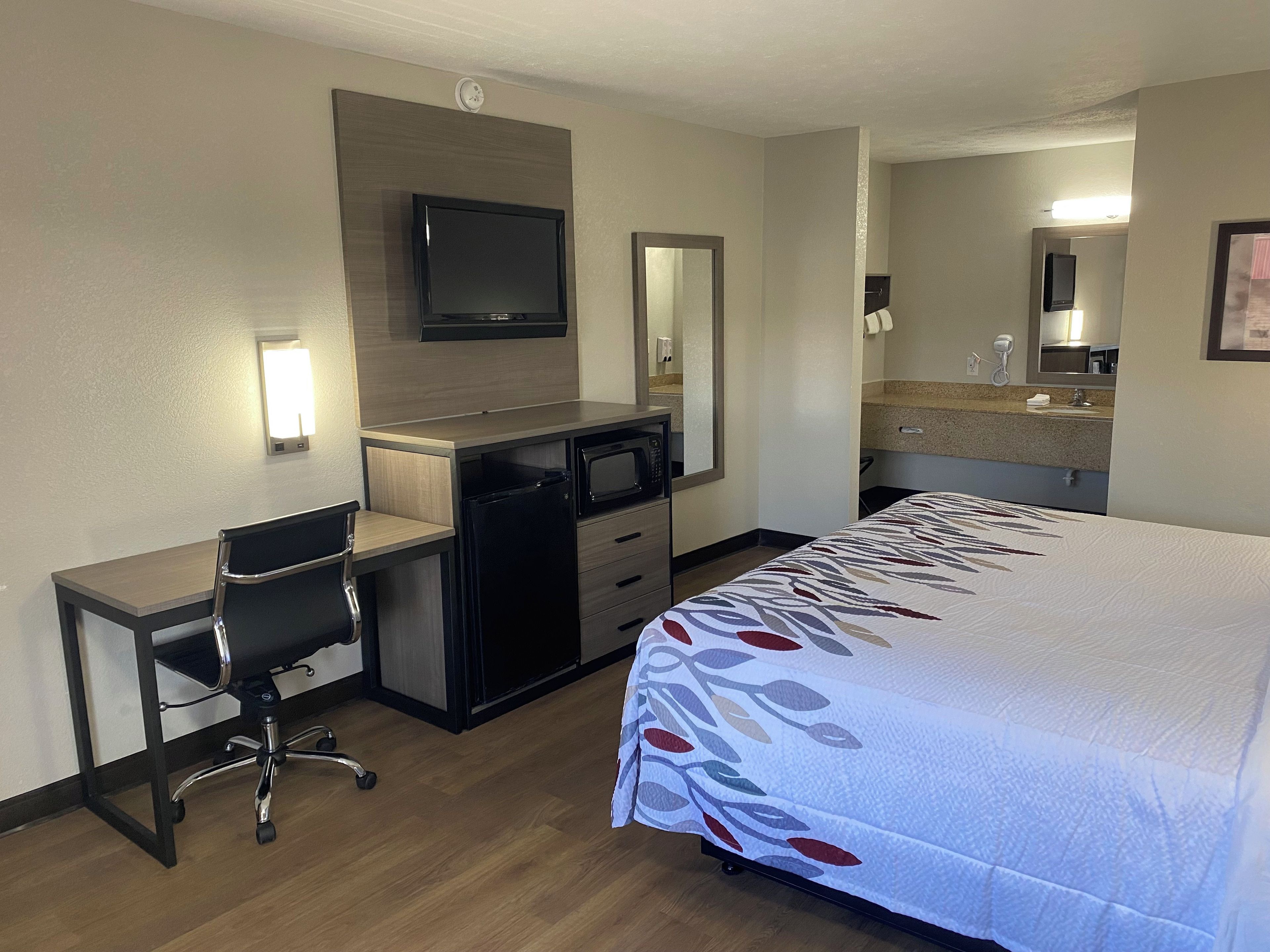 Une chambre d’hôtel équipée d’un lit, d’un bureau, d’une chaise, d’une télévision, d’un four à micro-ondes et d’une salle de bain avec un lavabo et un miroir.