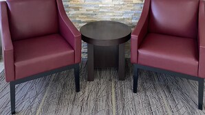 A Red Roof Inn sign on a stone wall with two red leather chairs and a small round table in front. - Red Roof Inn Jacksonville, AL  (Jacksonville)