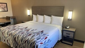 A hotel room with a bed, bedside tables, a desk, and a chair. - Red Roof Inn Jacksonville, AL  (Jacksonville)