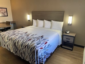A hotel room with a bed, bedside tables, a desk, and a chair. - Red Roof Inn Jacksonville, AL  (Jacksonville)