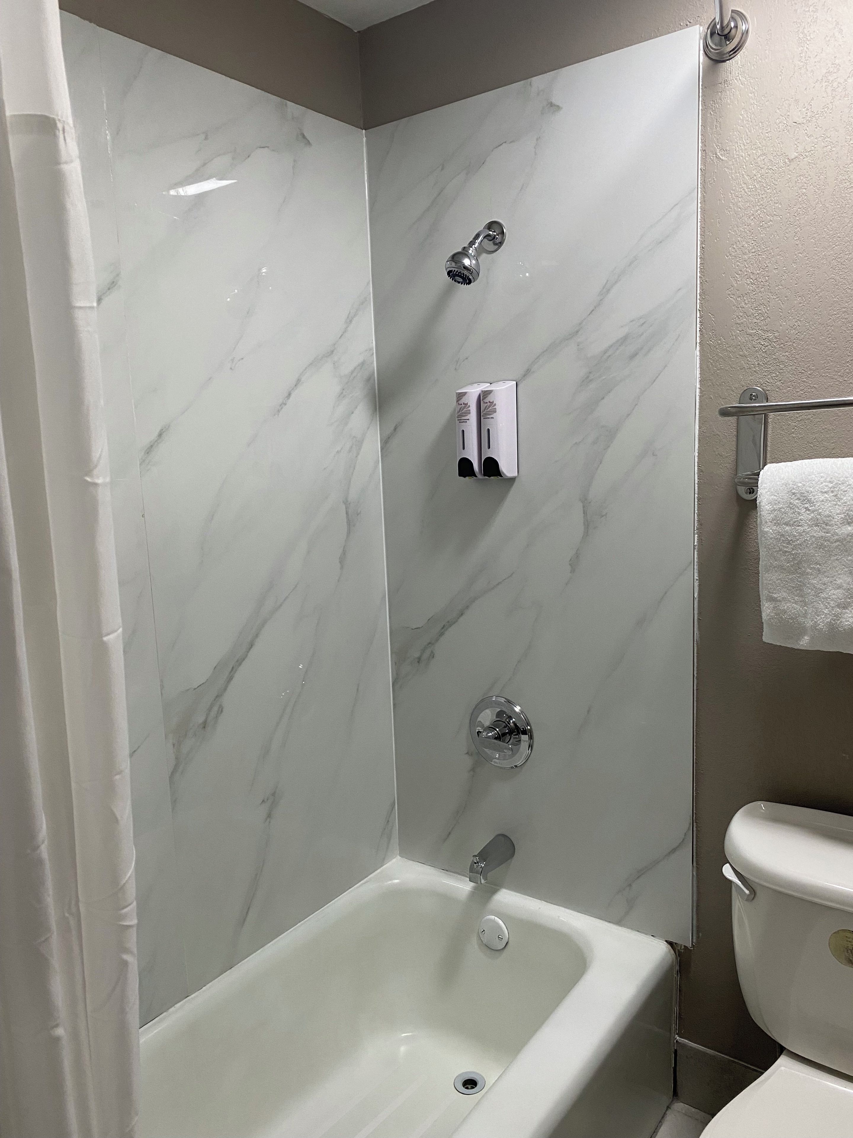 A bathroom with a bathtub, a toilet, and a shower area with a marble wall.