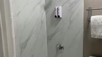 A bathroom with a bathtub, a toilet, and a shower area with a marble wall.