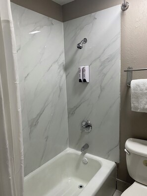 A bathroom with a bathtub, a toilet, and a shower area with a marble wall. - Red Roof Inn Jacksonville, AL  (Jacksonville)