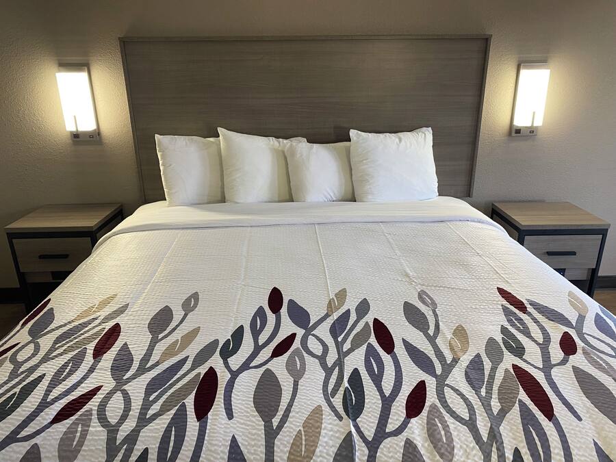 A hotel room with a bed, white bedding, a patterned bedspread, two bedside tables, and wall-mounted lights.