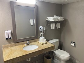 Un baño con lavamanos de granito, un espejo, un secador de pelo, un perchero para toallas y un inodoro.