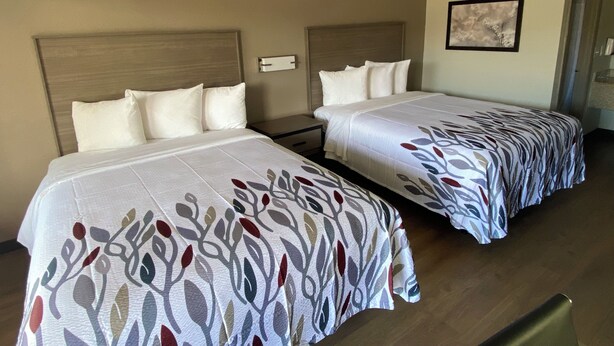 A hotel room with two beds, each with a headboard and pillows. There is a framed picture on the wall. - Red Roof Inn Jacksonville, AL  (Jacksonville)