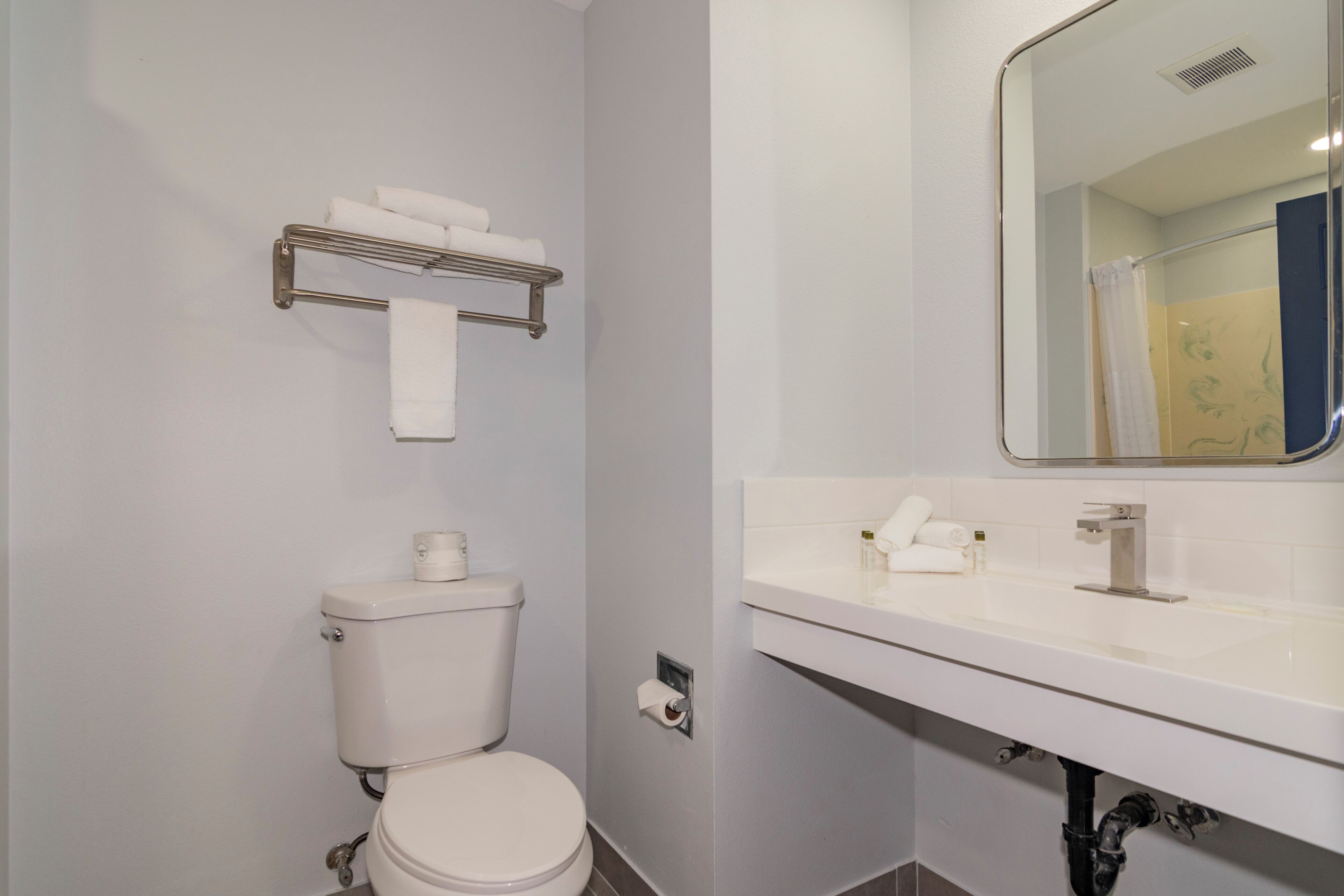 A bathroom with a toilet, a towel rack, a sink, and a mirror.