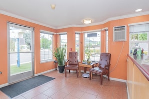 A reception area with a desk, two chairs, a potted plant, and a window with a view of the outside.