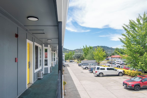 A hotel corridor with a green carpet, a yellow door, and a parking lot with various vehicles.