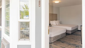A hotel room with a large window, a bed, a bedside table, and a carpeted floor.