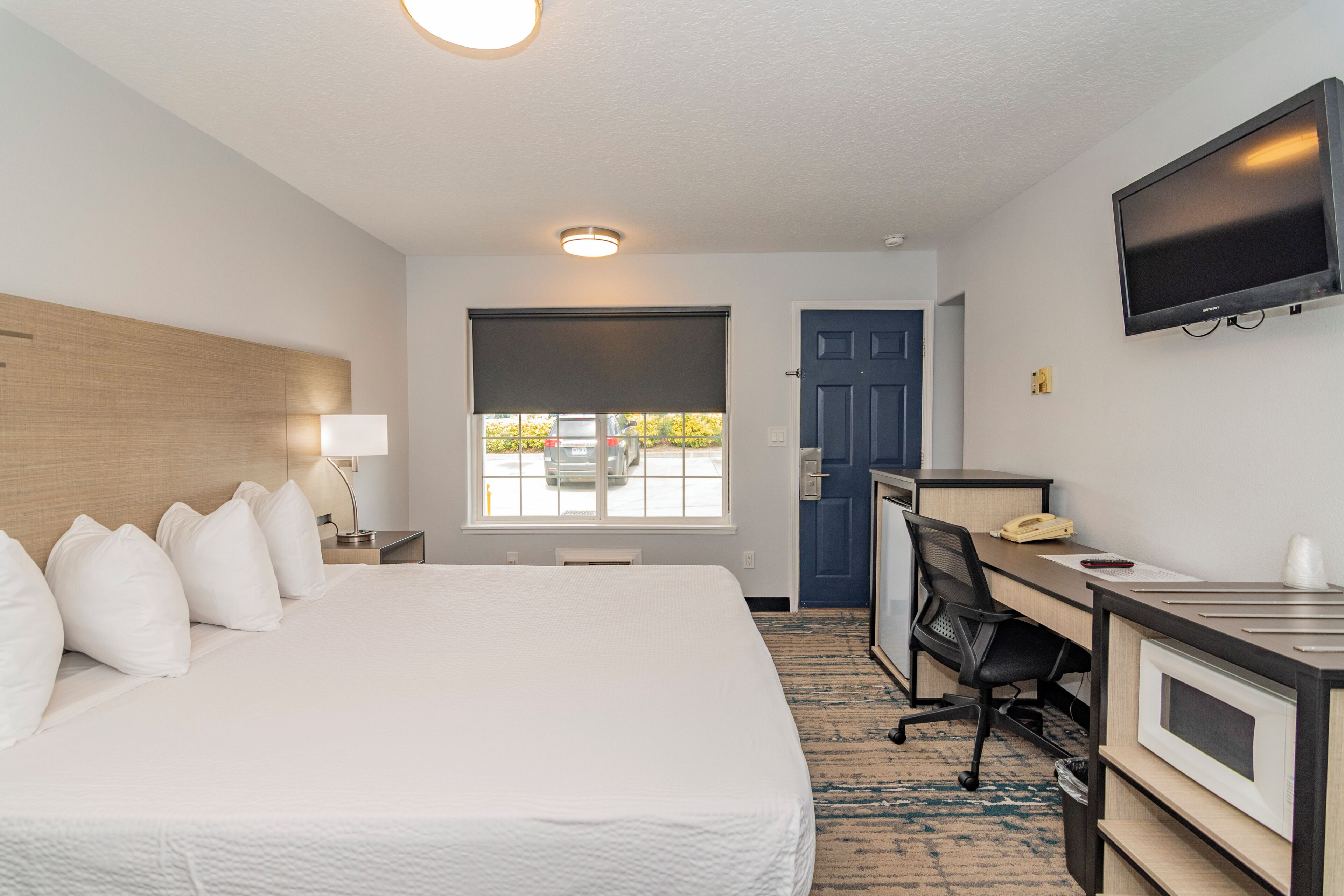 A hotel room with a bed, desk, television, and a window with a view of the street.