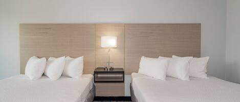 Une chambre d’hôtel avec deux lits, une table de chevet avec une lampe et une tête de lit.