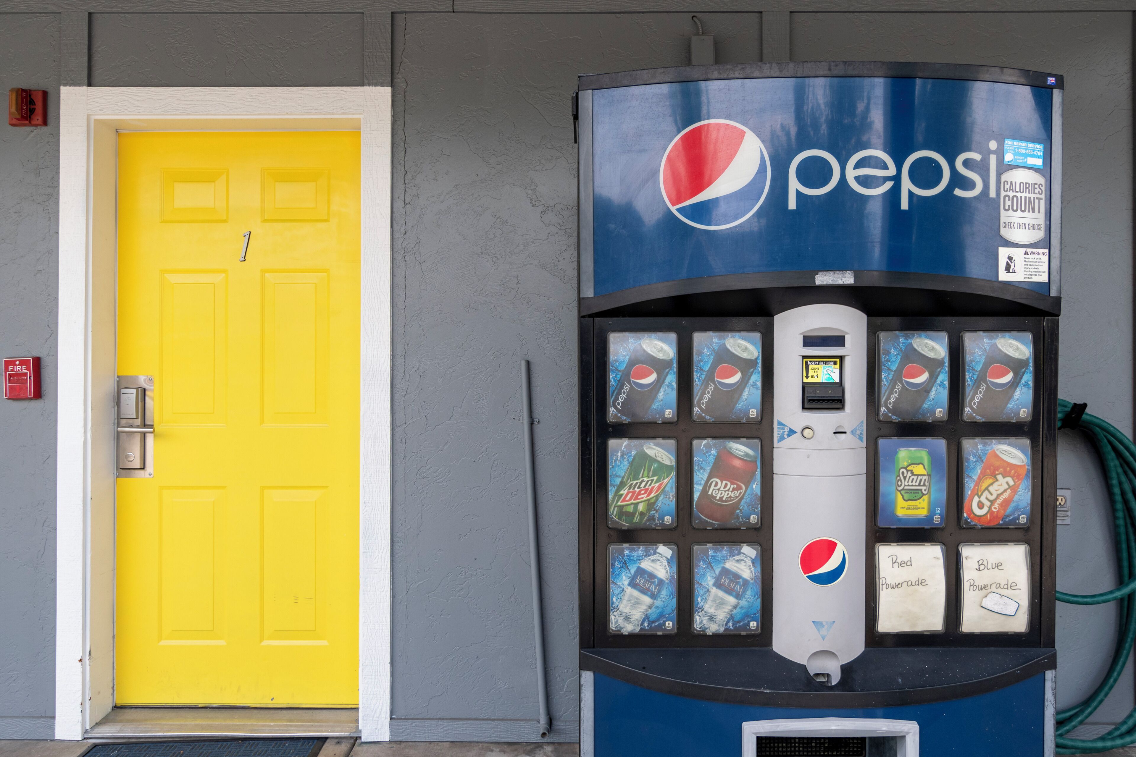 A vending machine with Pepsi products, a yellow door, and a fire alarm.