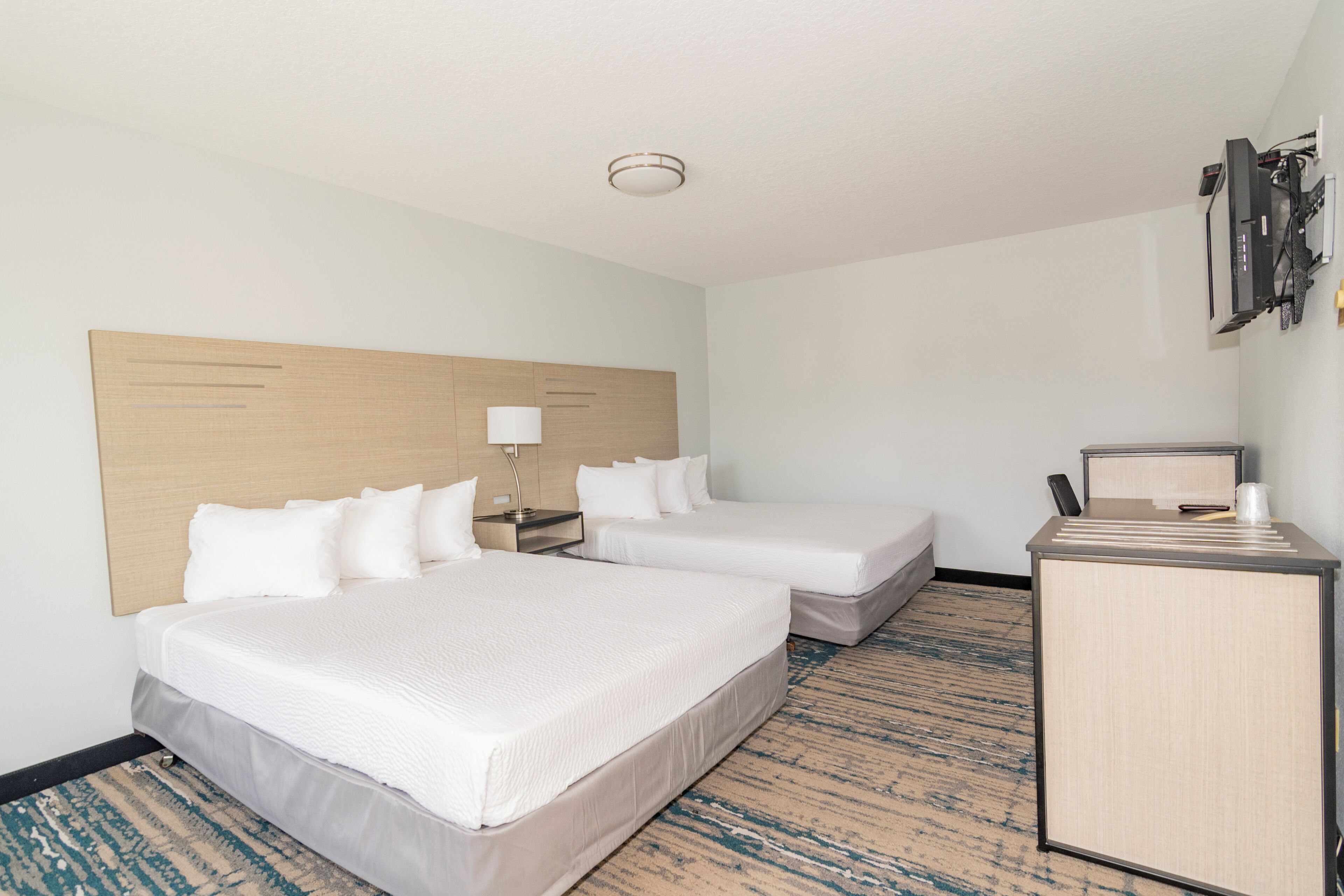 A hotel room with two beds, a desk, a lamp, and a television.