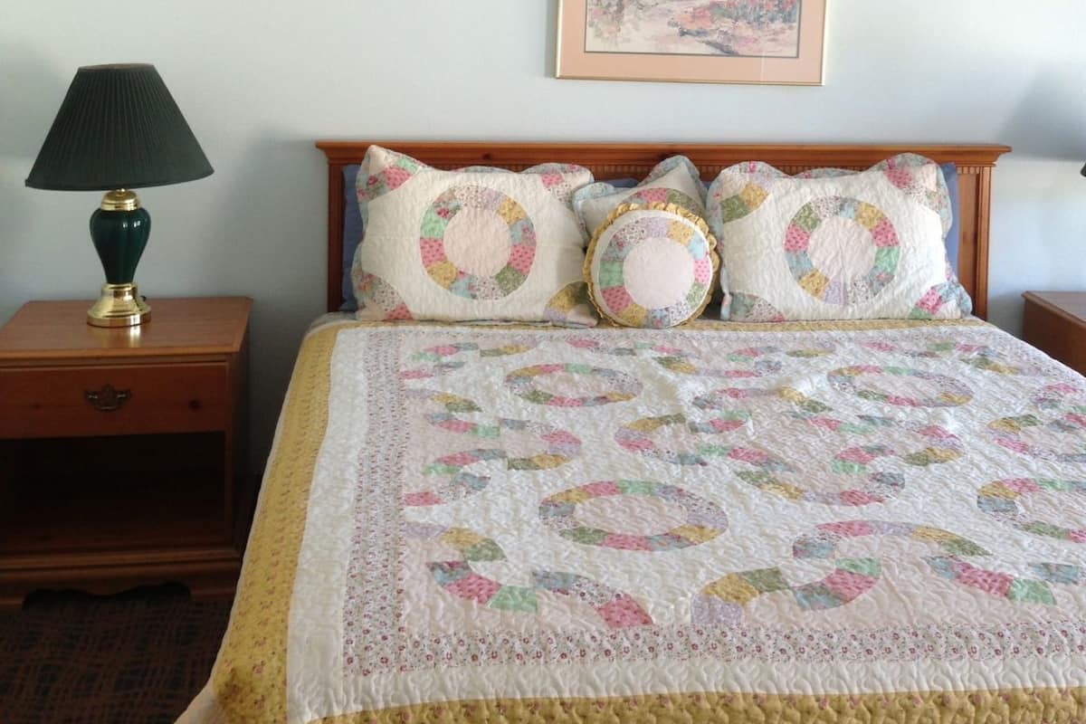 A bedroom with a floral-patterned bedspread, a framed picture above the bed, a nightstand with a lamp, and a wall with a floral border.