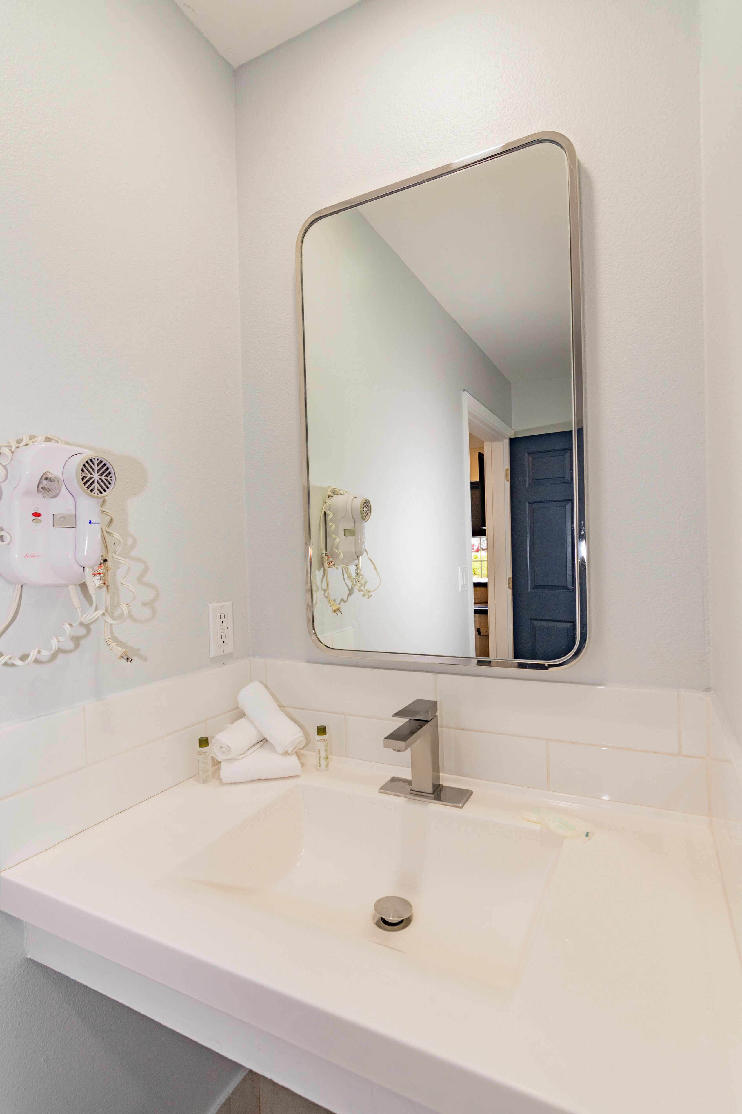Une salle de bain avec un lavabo blanc, un miroir et un sèche-cheveux fixé au mur.