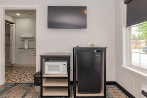 A hotel room with a flat-screen TV mounted on the wall, a compact refrigerator, a microwave, and a trash bin.