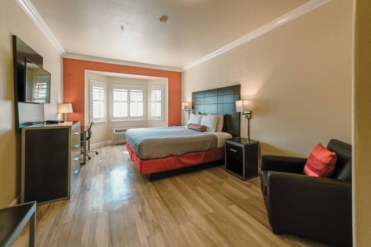 A hotel room with a bed, bedside tables, a desk, a chair, and a large window.