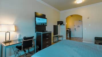 Habitación de hotel con cama, escritorio, silla, televisión, armario y baño visible a través de un arco.