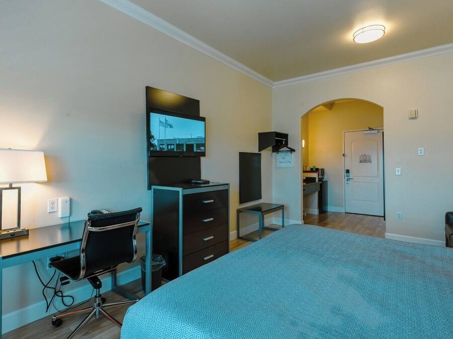 A hotel room with a bed, desk, chair, TV, wardrobe, and a bathroom visible through an archway.