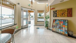 A hotel lobby with a glass door entrance, a reception desk, a large window, and a wall display of brochures. - Gateway Inn & Suites San Francisco SFO Airport (San Bruno)
