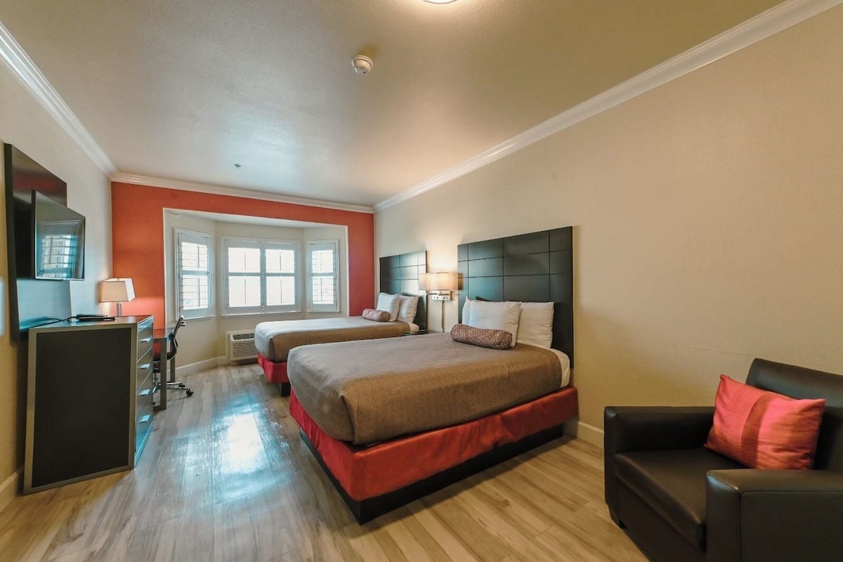 A hotel room with two beds, a desk, a chair, and a large window.