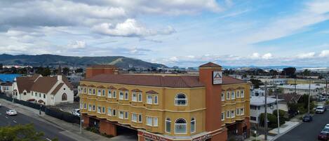 A hotel with a prominent red roof and yellow facade, located at a street corner with a clear view of the surrounding urban area and mountains in the distance.