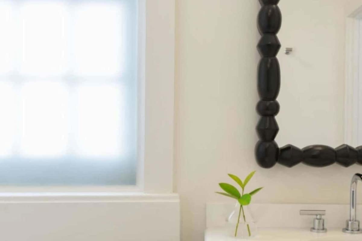 A bathroom with a white sink, a mirror with a black frame, and a window.
