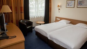 A hotel room with a desk, two beds, a chair, a small table, and a window with curtains. - Fletcher Hotel Steenwijk (Steenwijk)