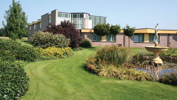 A modern building with a well-maintained garden, including a fountain and various plants. - Fletcher Hotel Steenwijk (Steenwijk)