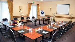 A conference room with long tables, chairs, and a projector screen. - Fletcher Hotel Steenwijk (Steenwijk)