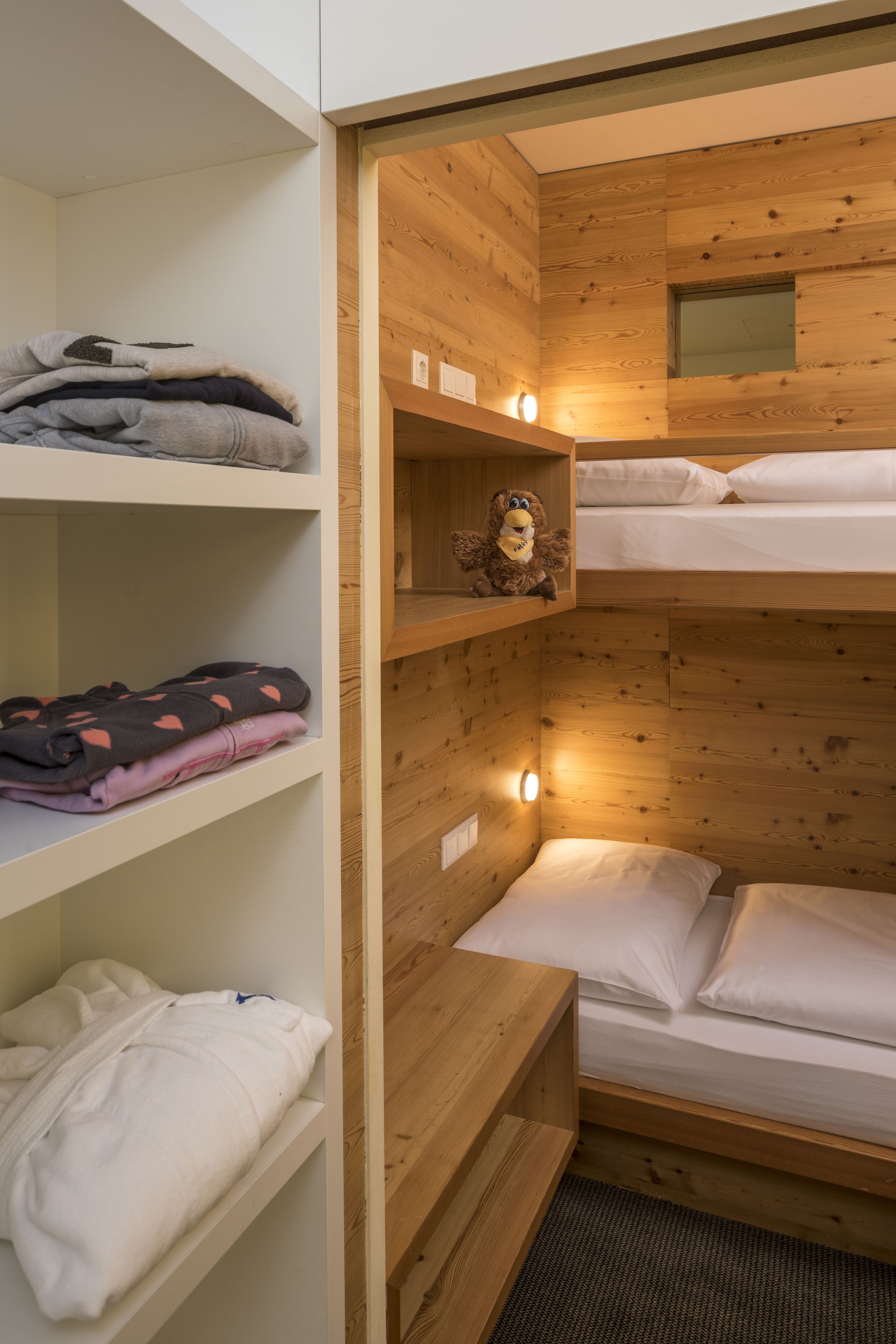 Habitación pequeña con literas, paredes de madera y estantes con ropa doblada.