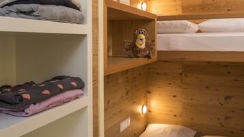Habitación pequeña con literas, paredes de madera y estantes con ropa doblada.