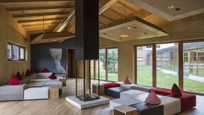 A modern living room with a large fireplace, wooden beams, and large windows offering a view of the outdoors. - Falkensteiner Club Funimation Katschberg (Rennweg am Katschberg)