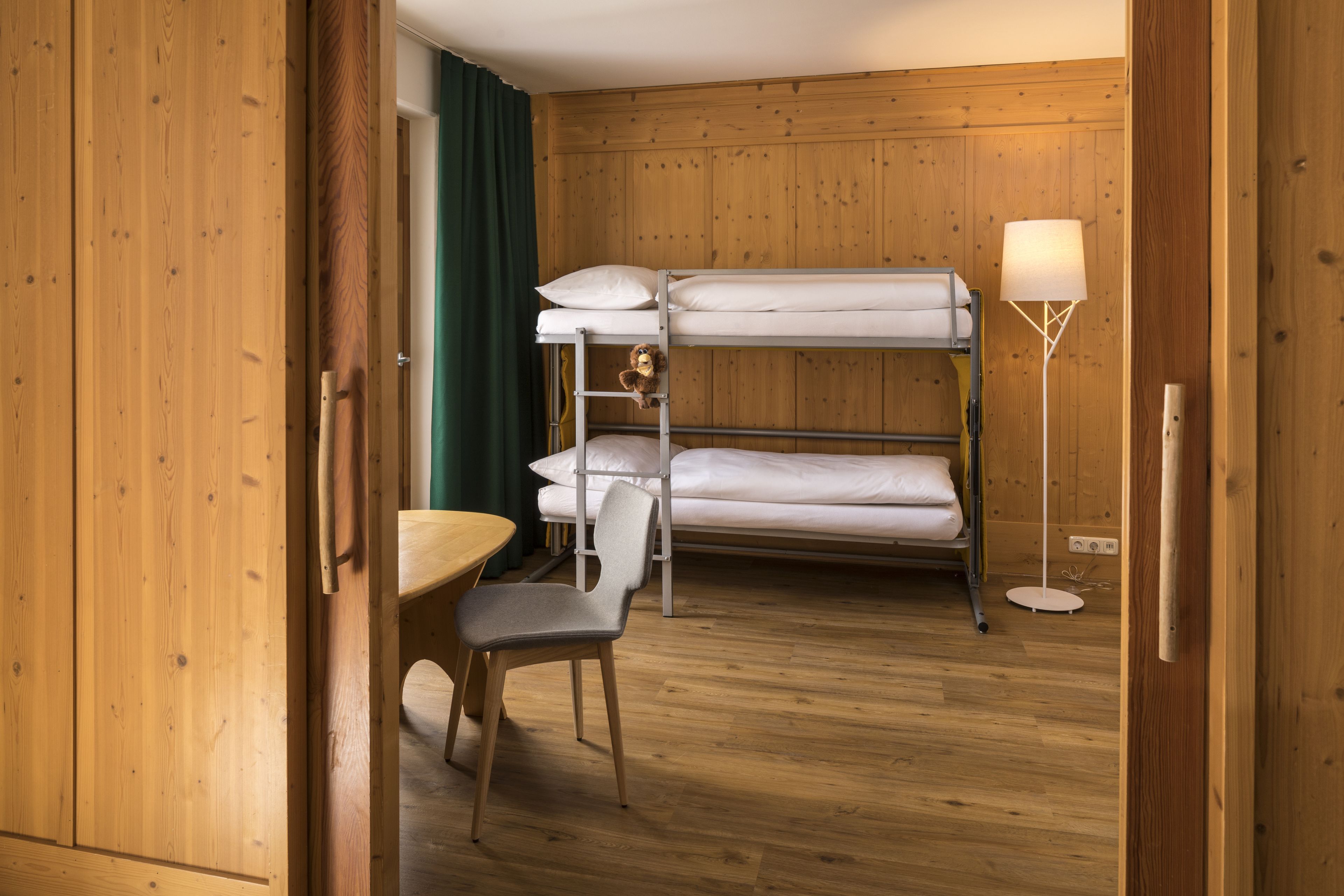 A bunk bed room with a desk and chair, wooden walls, and a floor lamp.