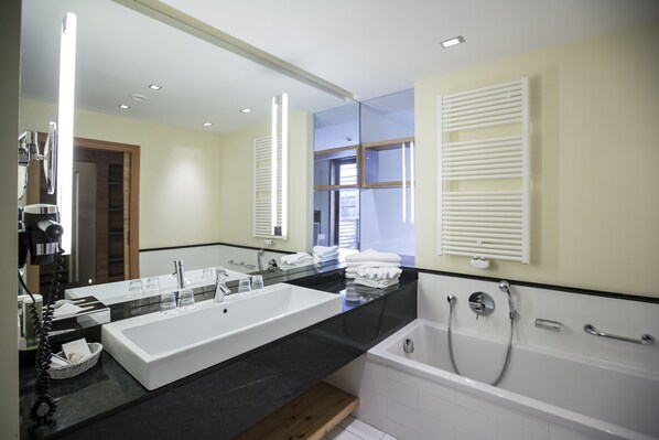 Un baño moderno con un lavamanos grande blanco, una bañera con dos cabezales de ducha y un espejo sobre el lavamanos.