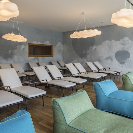 A room with multiple lounge chairs and sofas, a television mounted on the wall, and cloud-shaped ceiling lights.