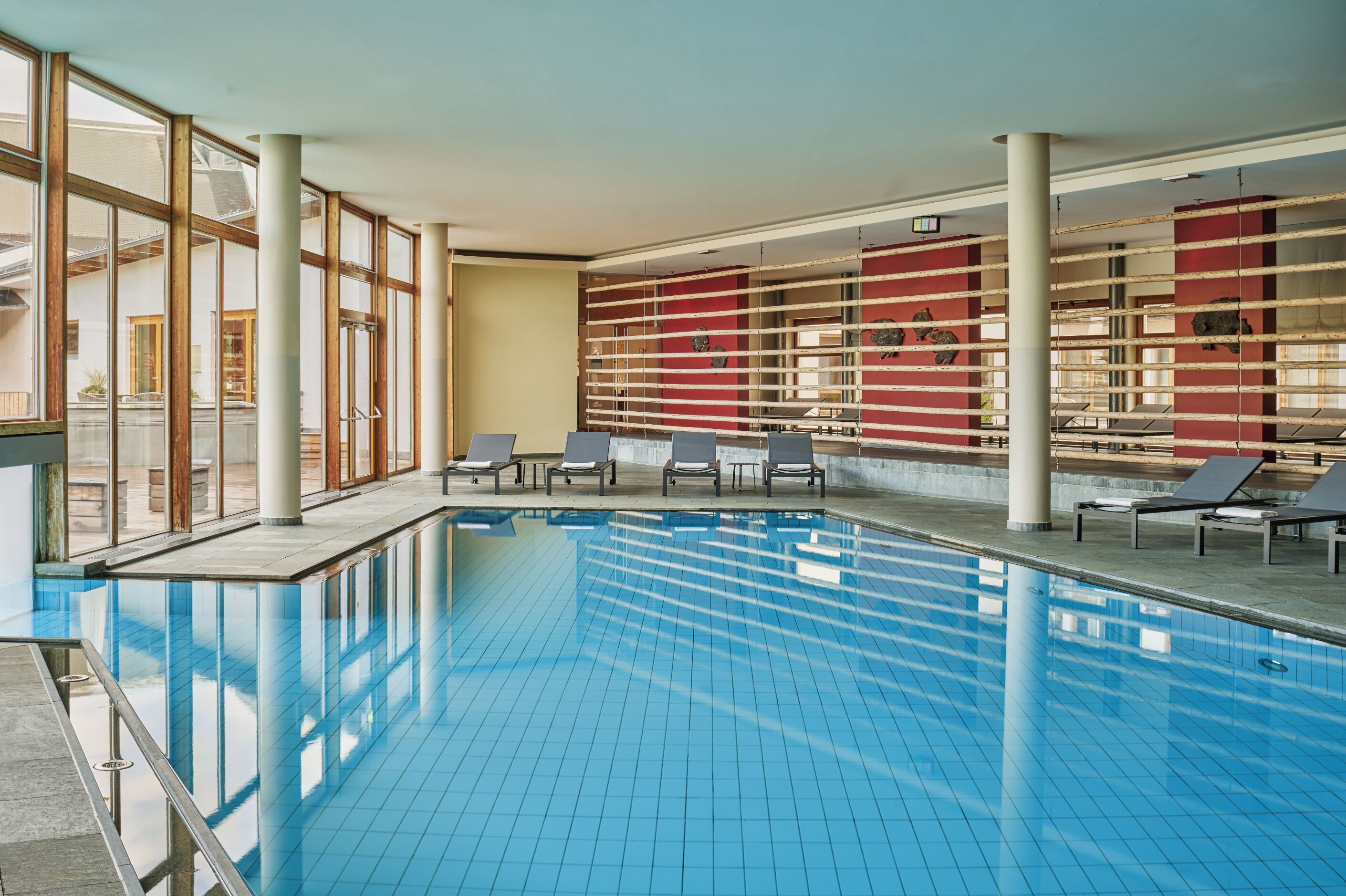 Une piscine intérieure à l’eau d’un bleu cristallin, entourée de chaises longues et bordée d’un mur rouge orné d’œuvres d’art.