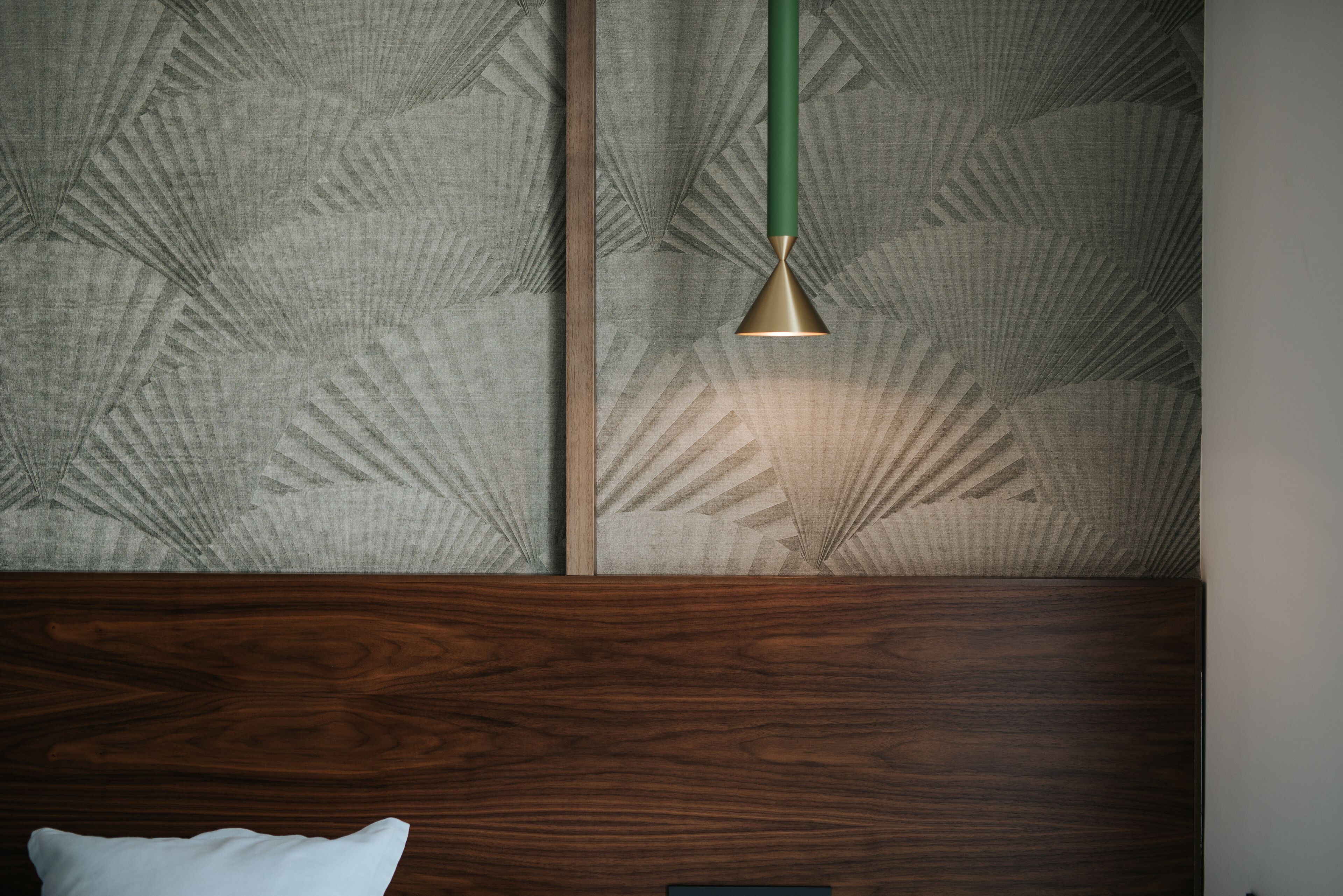 Een kamer met een behang met patroon, een houten hoofdeinde en een groene hanglamp.