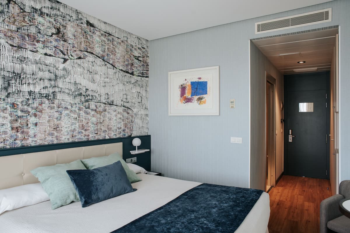 Un cuarto de hotel con una cama grande, un cabecero con un diseño decorativo, una pared con una obra de arte texturizada y un cuadro enmarcado.
