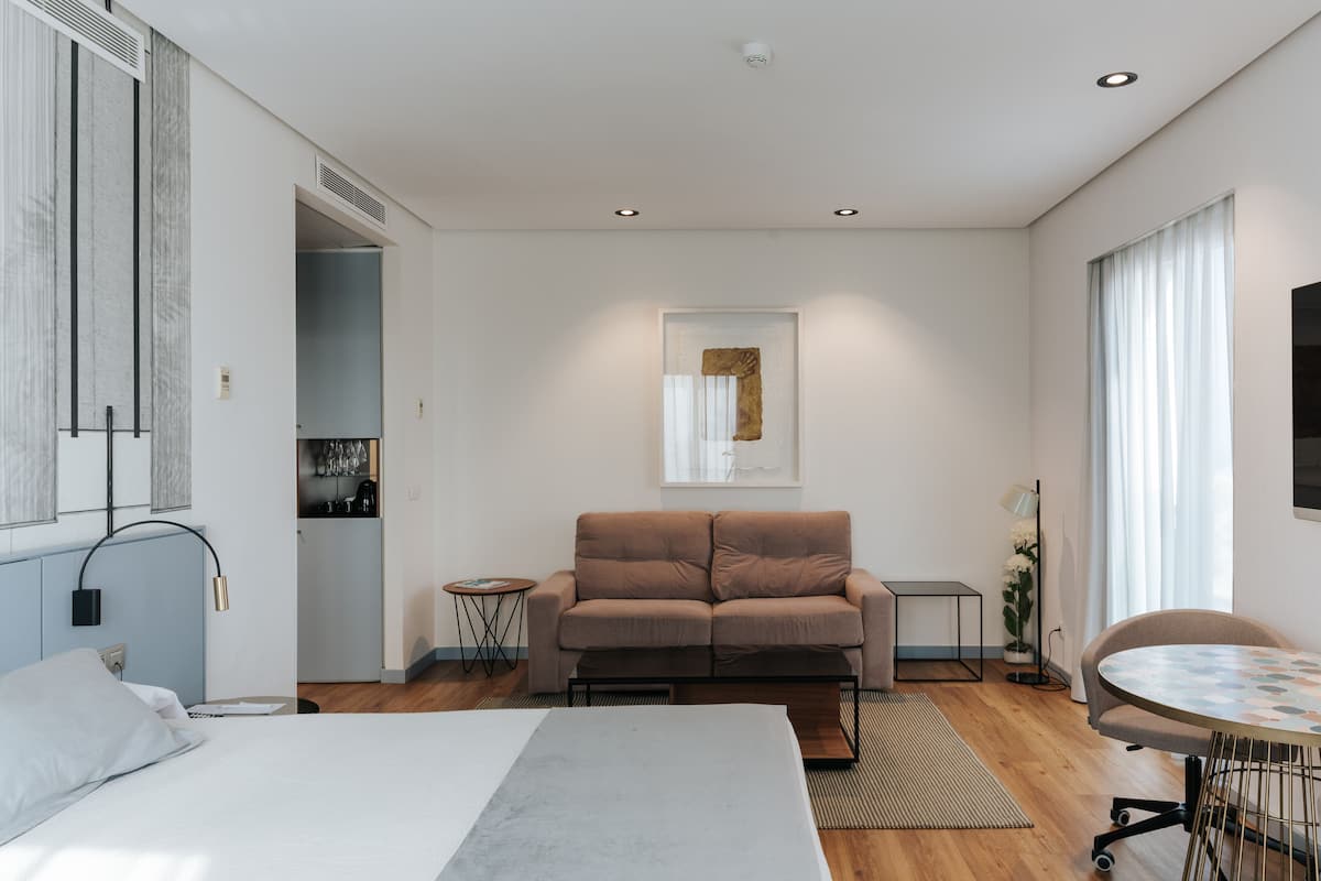 Una habitación de hotel moderna con cama, sofá, mesa de comedor y zona de cocina.