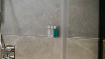 A bathroom with a marble wall, a shower area, and a shelf with toiletries.