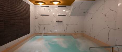 Un cuarto de spa con pared de mármol, banca de madera y una pequeña cascada.