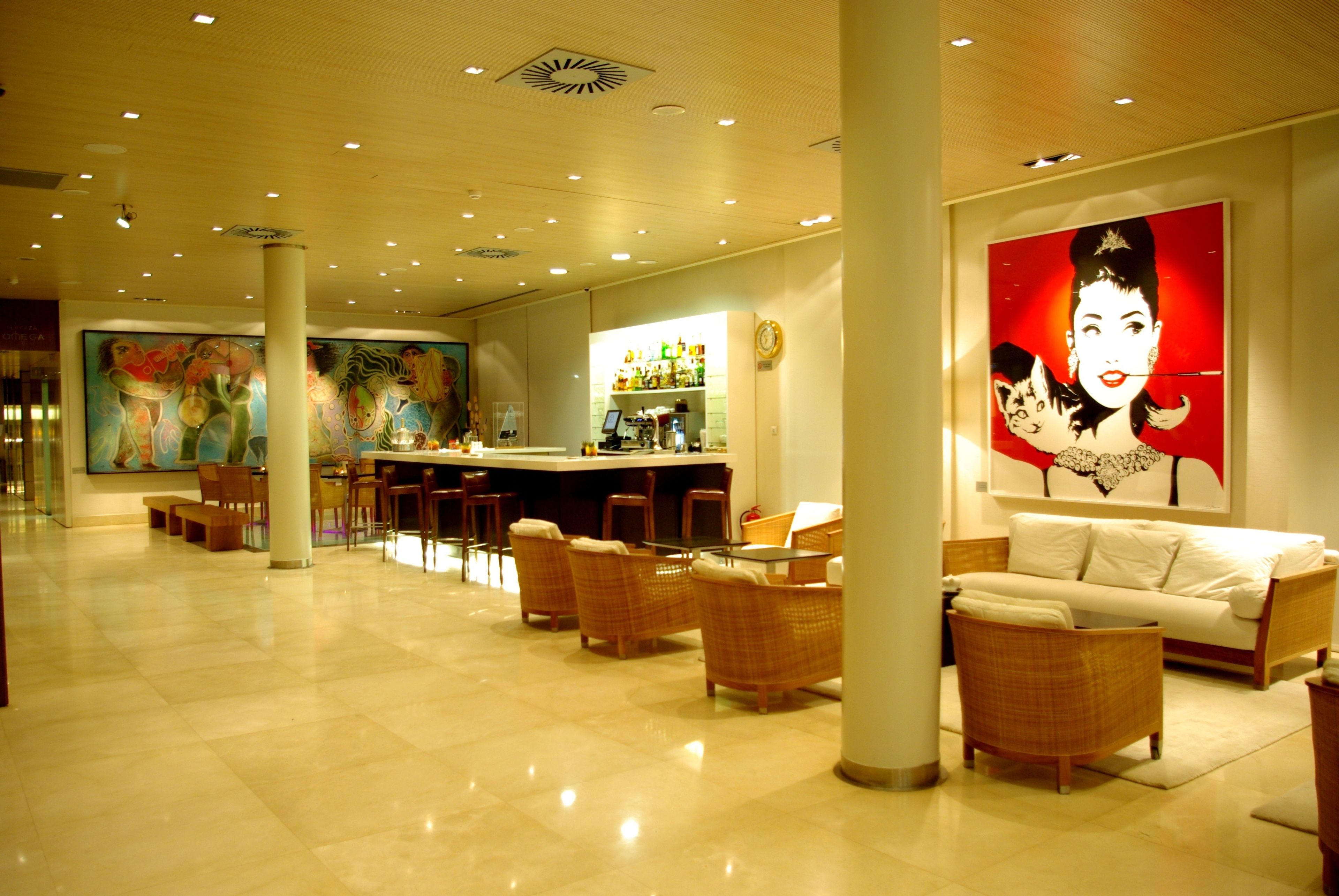 A hotel lobby with a bar area, wicker furniture, and a large painting on the wall.