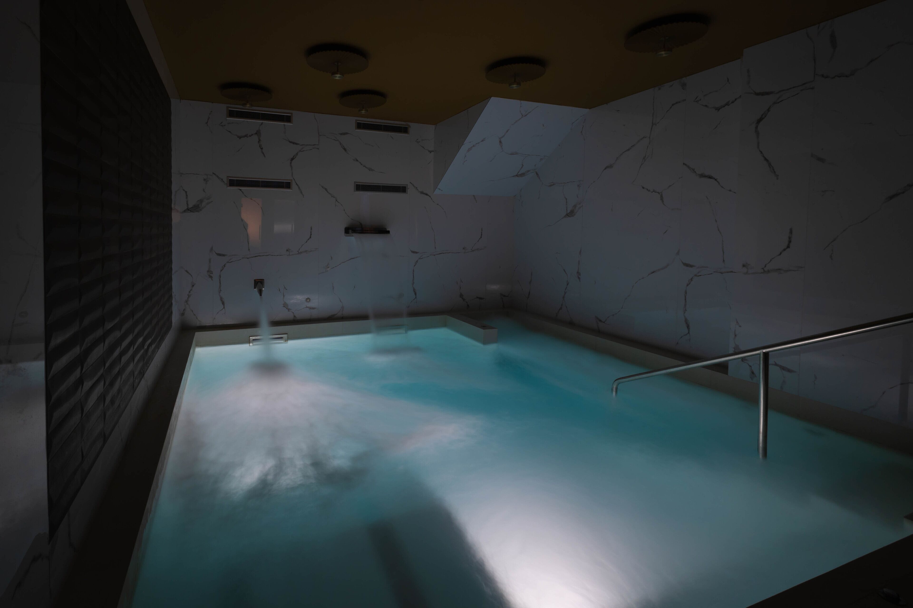 Una piscina con diseño moderno, que presenta una textura de pared similar al mármol y un tragaluz superior.