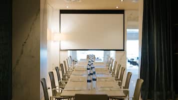 A conference room with a long table, chairs, a projector screen, and a window with a view of cows.